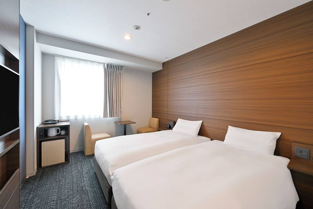 A hotel room with two beds, a desk, a chair, and a TV.