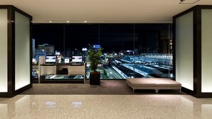 A modern hotel lobby with a large glass wall offering a nighttime city view, a reception desk, and a seating area with a potted plant. - JR WEST GROUP VIA INN OKAYAMA (Okayama)