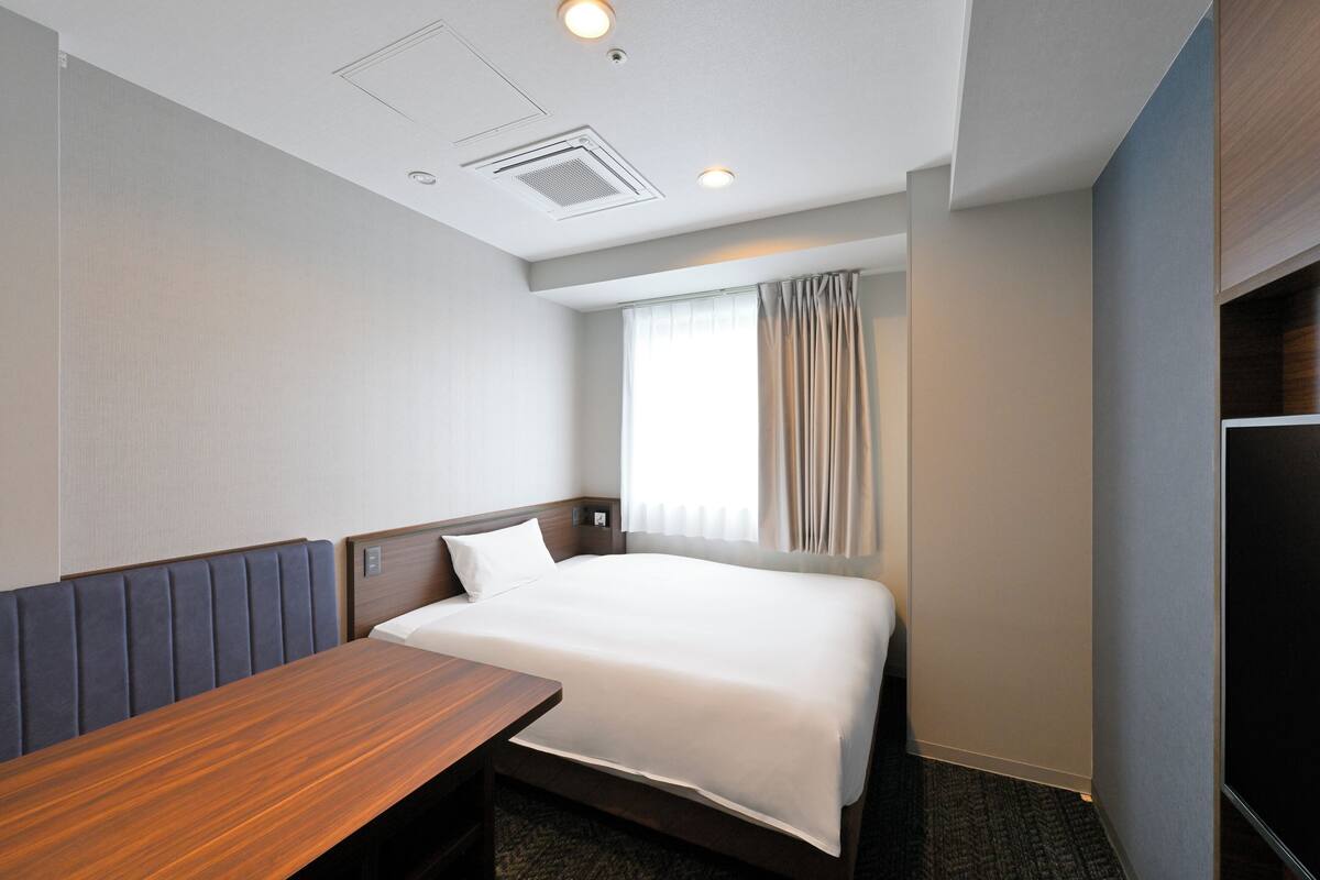 A hotel room with a single bed, a wooden desk, and a window with curtains.