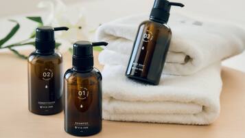 Três frascos de produtos de higiene corporal rotulados 01, 02 e 03, com uma toalha branca dobrada sobre uma superfície de madeira.