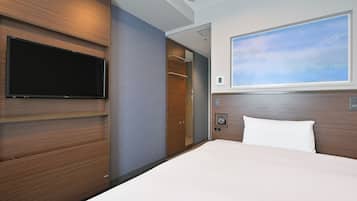 A hotel room with a bed, a mounted TV, a large window with a view, and a wooden headboard.