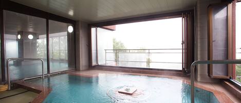 Una piscina interior con paredes de vidrio transparente, suelo de baldosas y vistas al exterior.