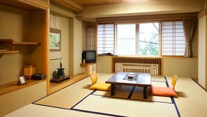 Una habitación japonesa tradicional con suelo de tatami, una mesa baja con cojines, un televisor y una ventana con biombos shoji.