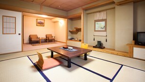 Una habitación japonesa tradicional con suelo de tatami, una mesa baja con cojines, un televisor y una puerta corrediza que da a otra habitación.
