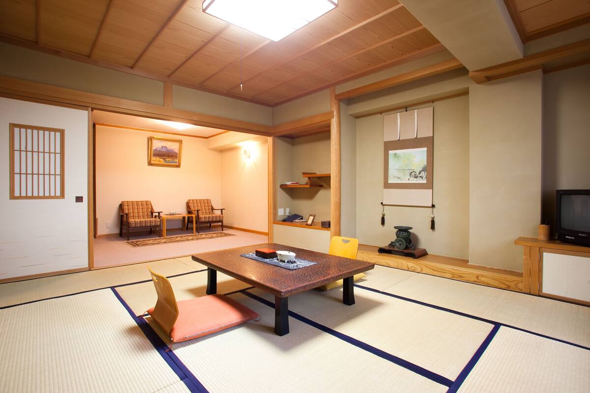 A traditional Japanese room with tatami flooring, a low table with cushions, a television, and a sliding door leading to another room.