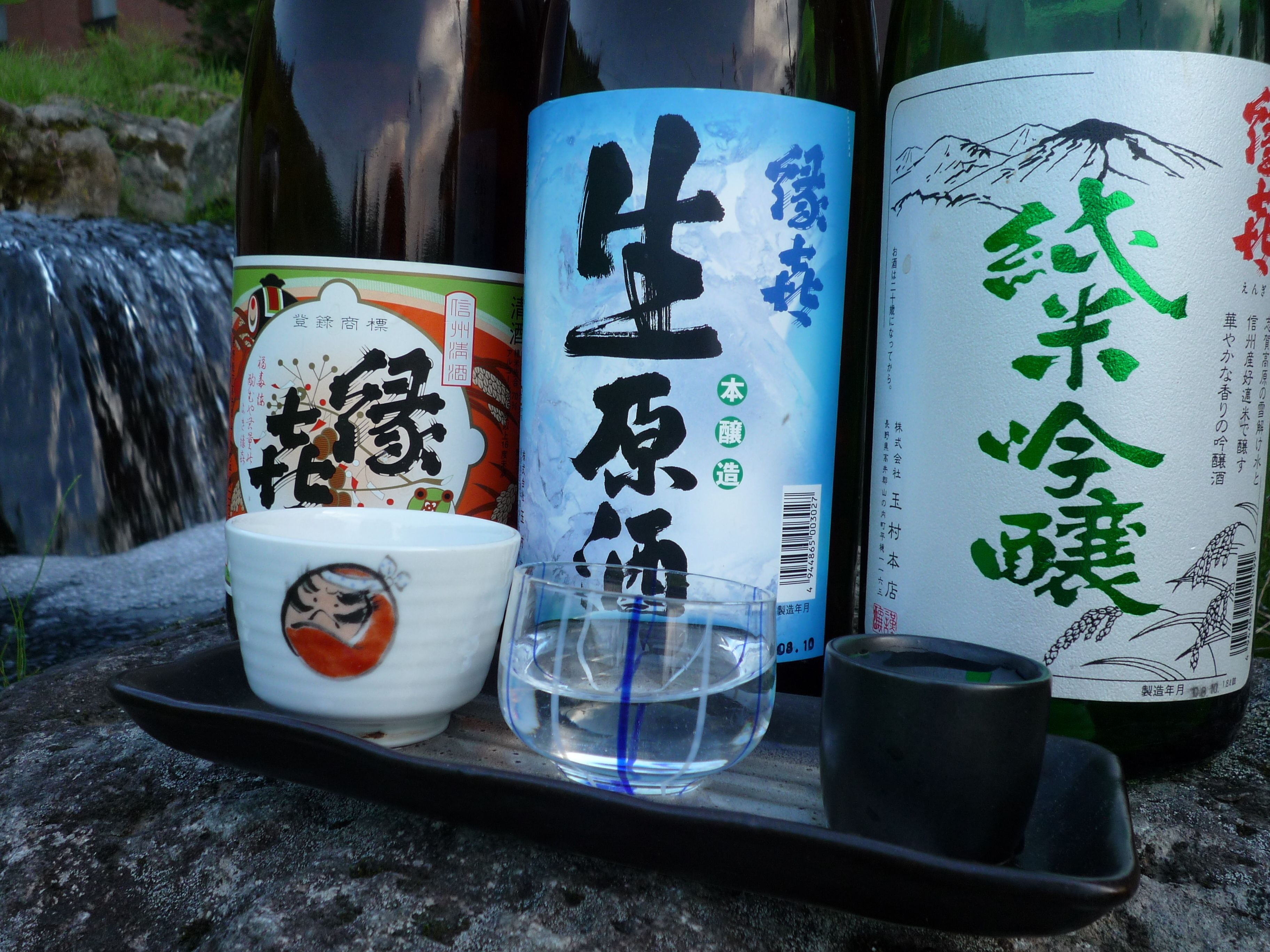 A tray with a bottle of sake, a bottle of water, a glass, and a ceramic cup with a design.
