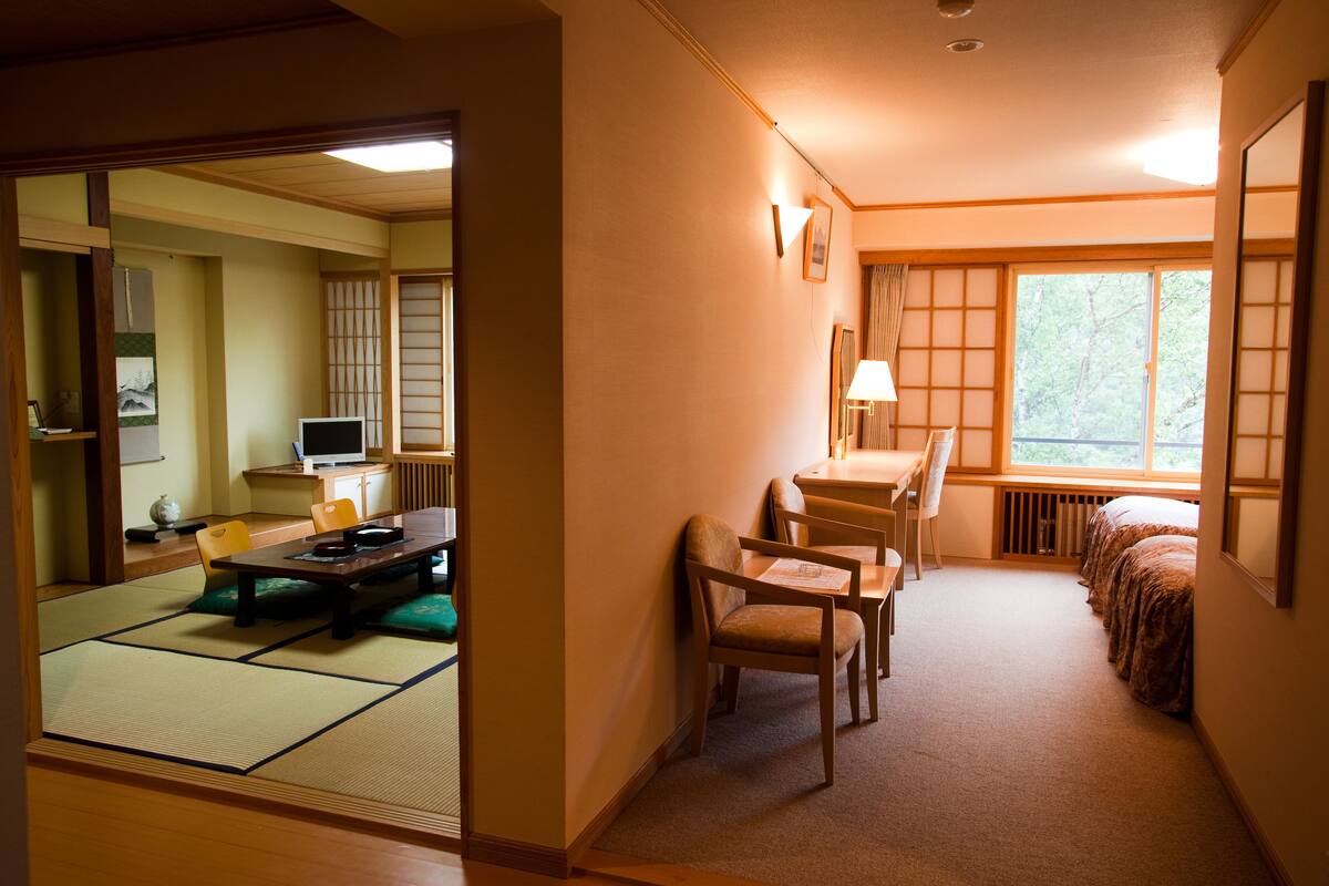 A traditional Japanese room with tatami flooring, a low table with cushions, a bed with a futon, and a sliding door leading to another room.