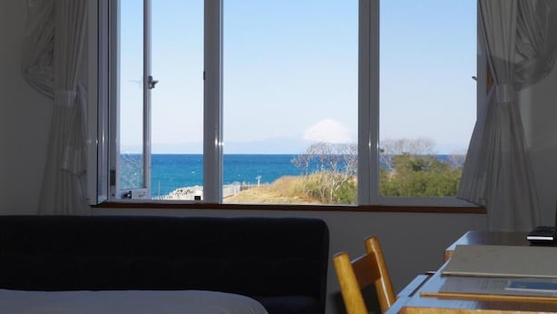 A room with a large window offering a view of the sea and a mountain. - Hotel Familio Tateyama (Tateyama)