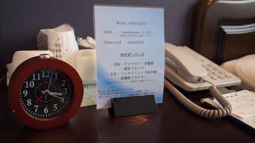 Une chambre d’hôtel équipée d’une horloge, d’un téléphone et d’une affiche indiquant les équipements disponibles, tels qu’un sèche-cheveux, la climatisation et le mot de passe du Wi-Fi.