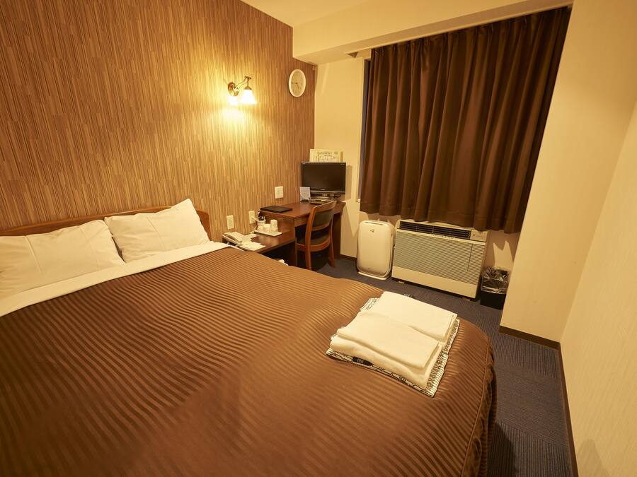 A hotel room with a large bed, a desk with a computer, a radiator, and a window with curtains.