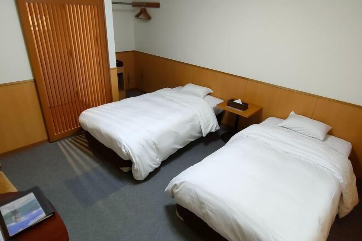Une chambre d’hôtel avec deux lits simples, une tête de lit en bois, une petite table de chevet et un bureau avec une chaise.