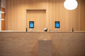 A reception desk with two digital screens displaying a welcome message, a cash register, and a small statue. - The Park Lodge Kamikochi (Matsumoto)