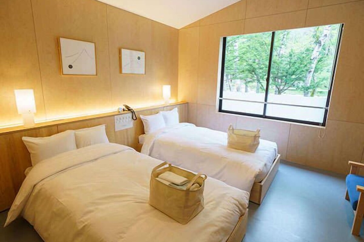 Une chambre d’hôtel avec deux lits, une grande fenêtre et une tête de lit en bois.