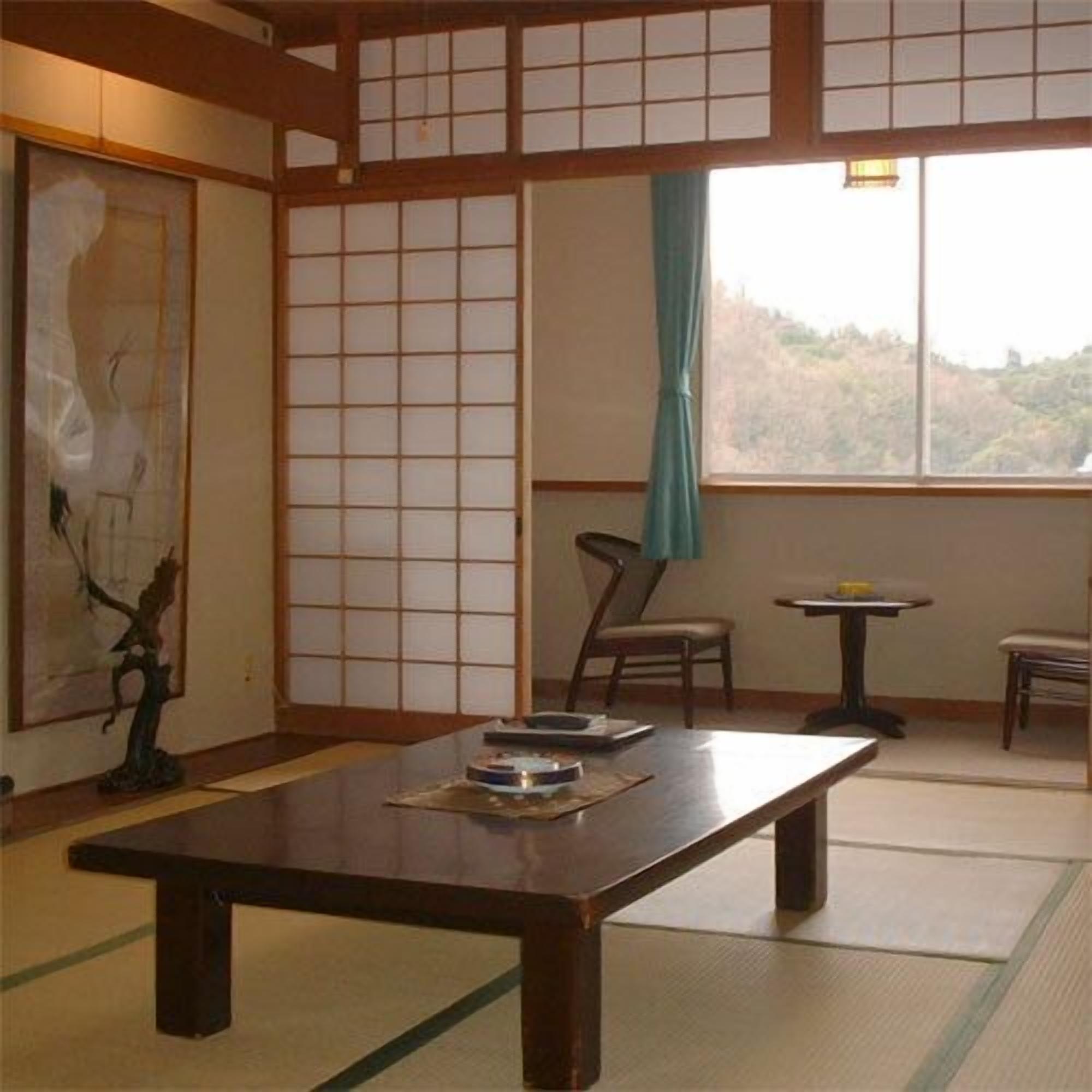 Een traditionele Japanse kamer met tatami vloeren, een lage tafel, een stoel en een schilderij aan de muur.