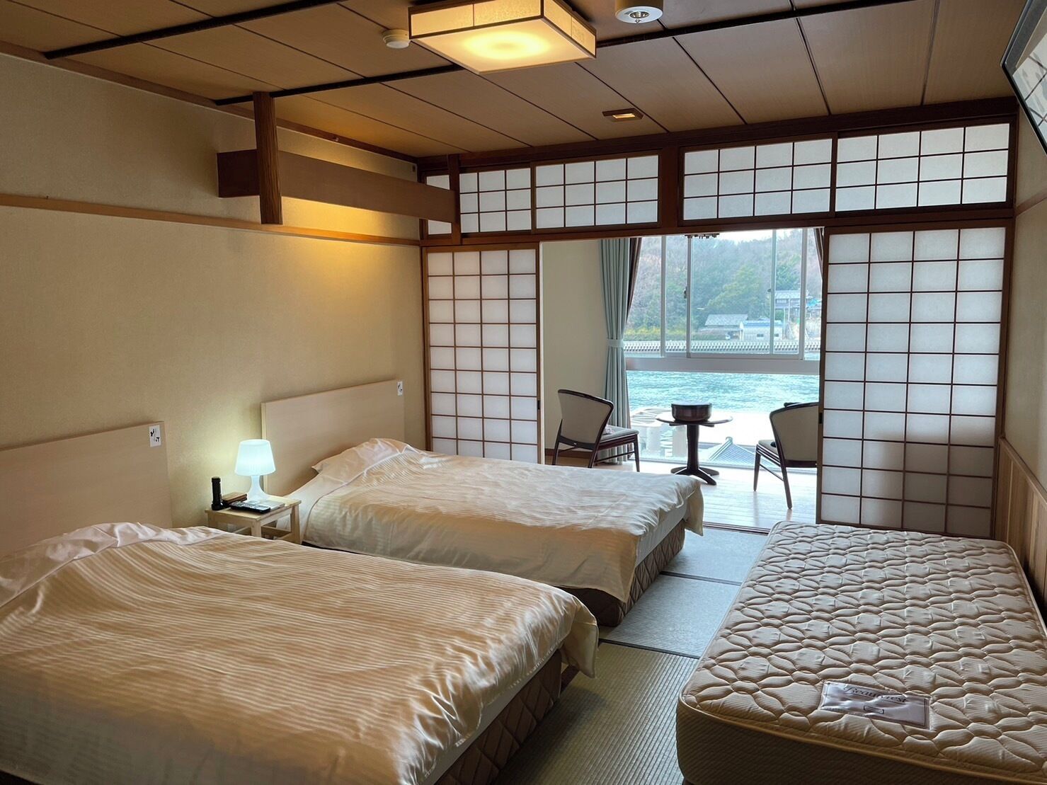 Hotelkamer met twee bedden, een tafeltje, stoelen, uitzicht op zee en traditionele Japanse schuifdeuren.