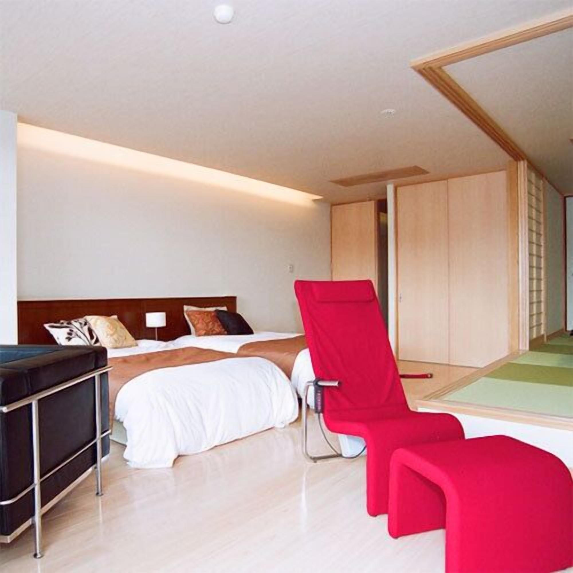 Een moderne hotelkamer met een bed, een rode stoel en een grote spiegel.