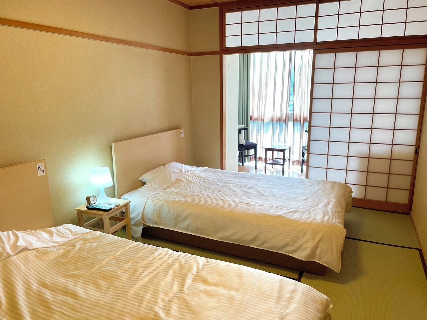 Een hotelkamer met twee bedden, een klein nachtkastje met een lamp en een schuifdeur van shoji-scherm.