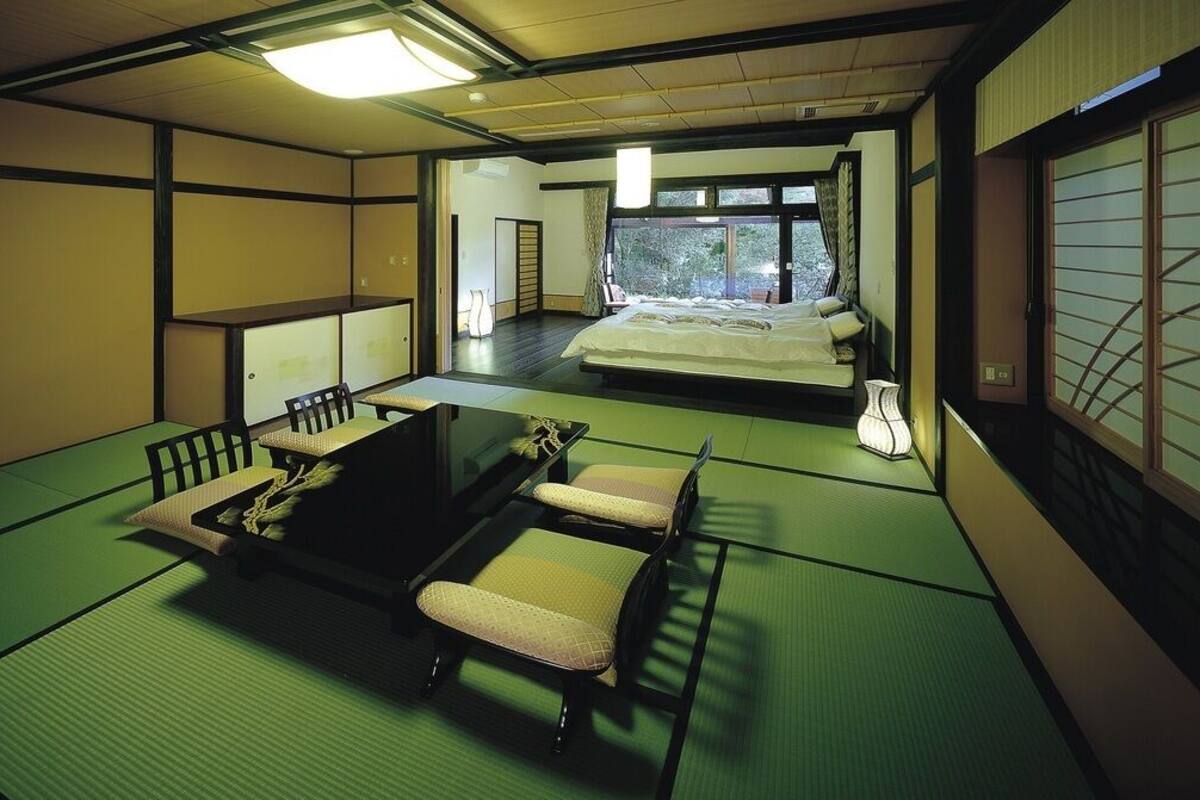 Ein traditioneller japanischer Raum mit Tatami-Bodenbelag, einem Futonbett, einem niedrigen Tisch mit Stuhl und einer Schiebetür.