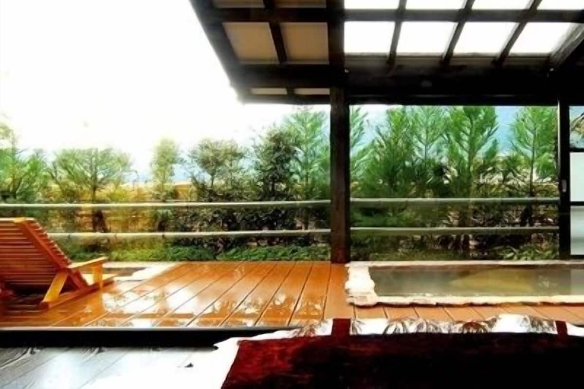 A wooden deck with a hot tub, a wooden chair, and a view of greenery.