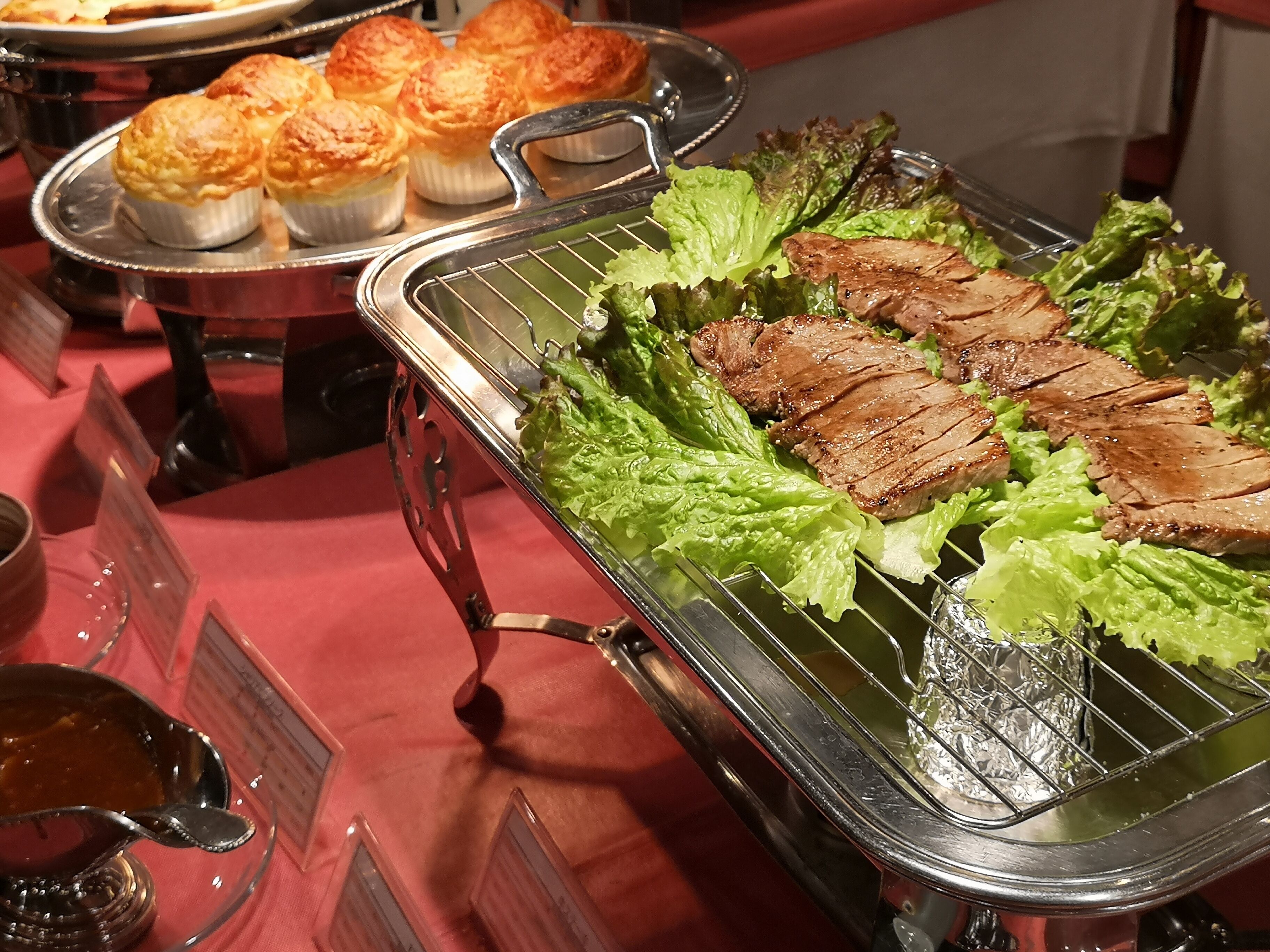A buffet with grilled meat, lettuce, and baked goods.