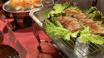 A buffet with grilled meat, lettuce, and baked goods.