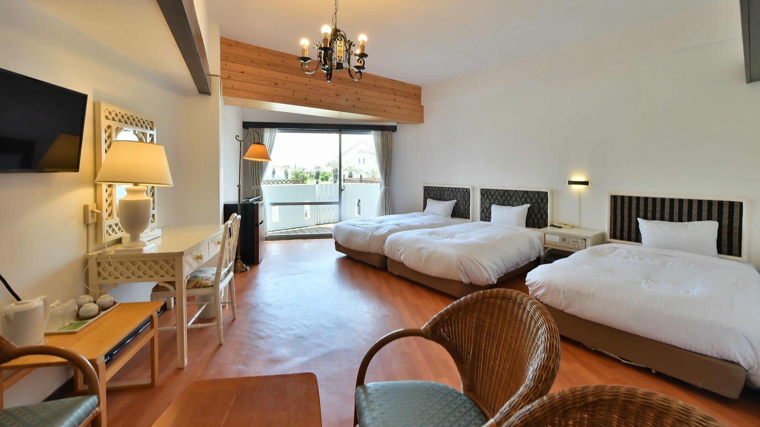 Camera d'albergo con due letti, una scrivania con lampada, una sedia, una televisione e un balcone con vista.