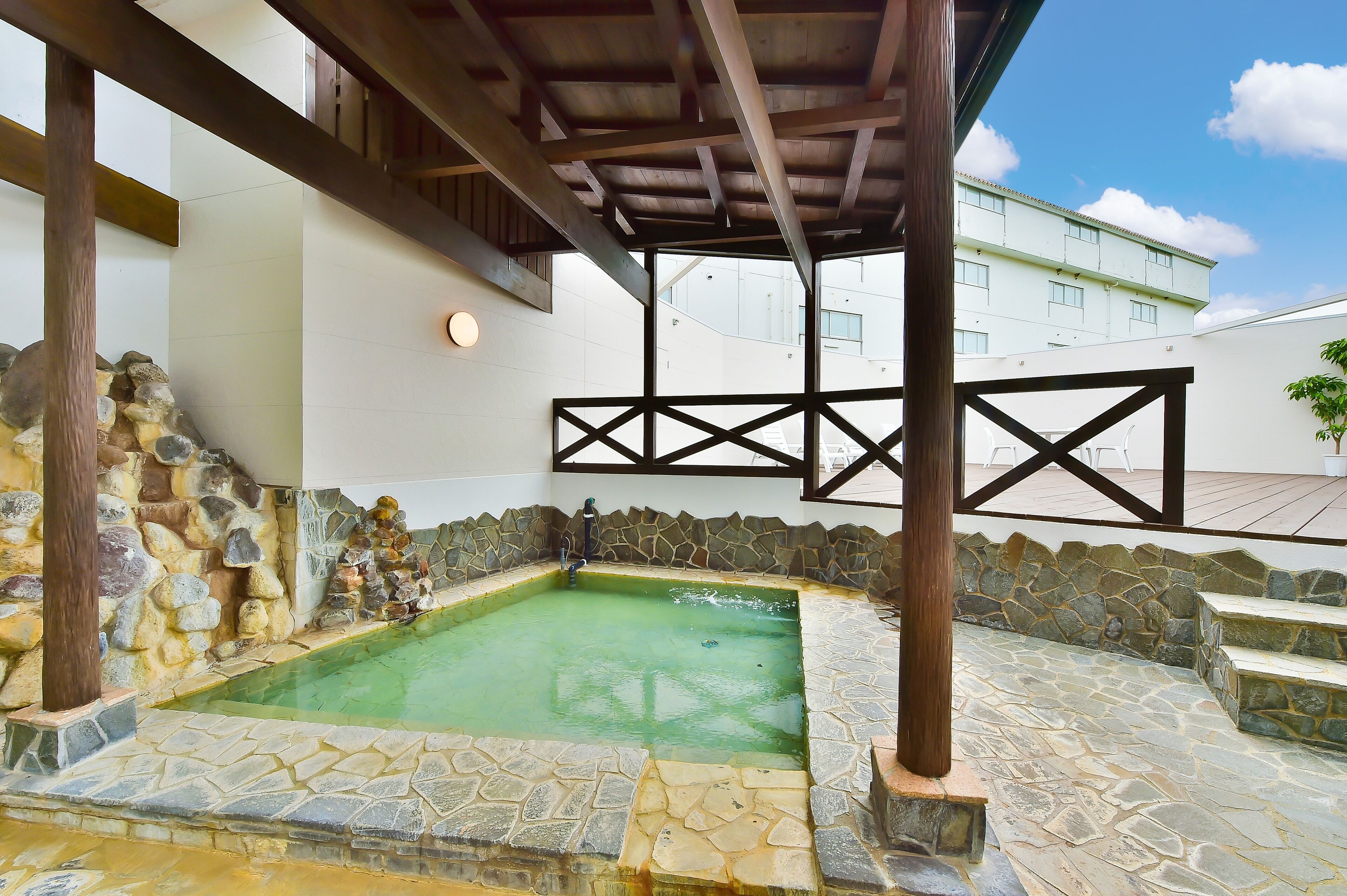 A stone pool with a wooden deck and a stone wall with a stone sculpture.