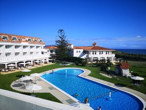 Ein Resort mit einem großen Schwimmbad, mehreren Gebäuden mit roten Ziegeldächern und Blick auf den Ozean.
