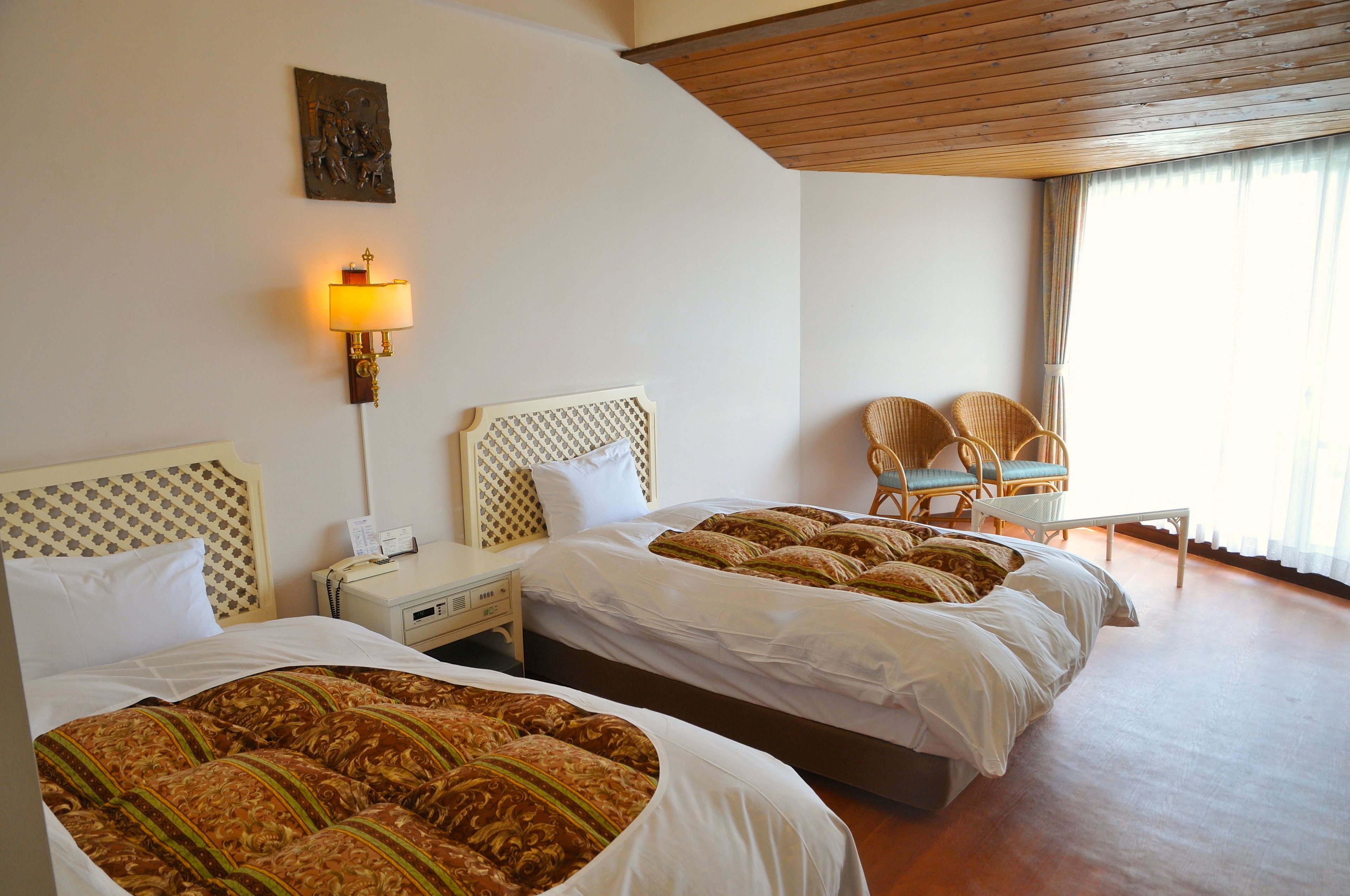 Una habitación de hotel con dos camas, una mesita de noche, una lámpara y sillones de mimbre.