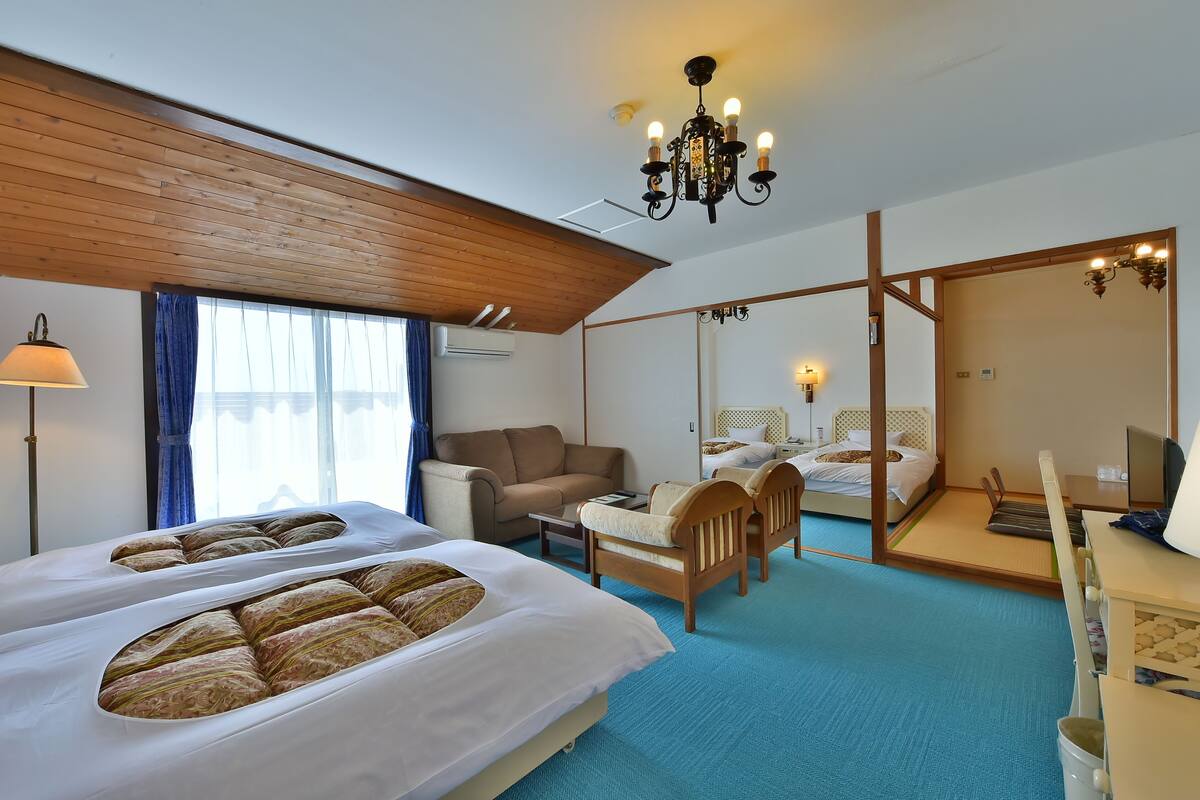 A hotel room with two beds, a sofa, a small table, and a TV.