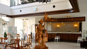 A lobby with wooden chairs, a reception desk, and a statue of a figure holding a staff. - Tateyama Resort Hotel (Tateyama)