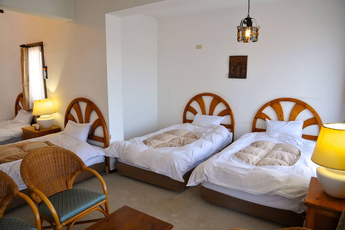 A hotel room with three single beds, wooden headboards, and a small table with a chair.