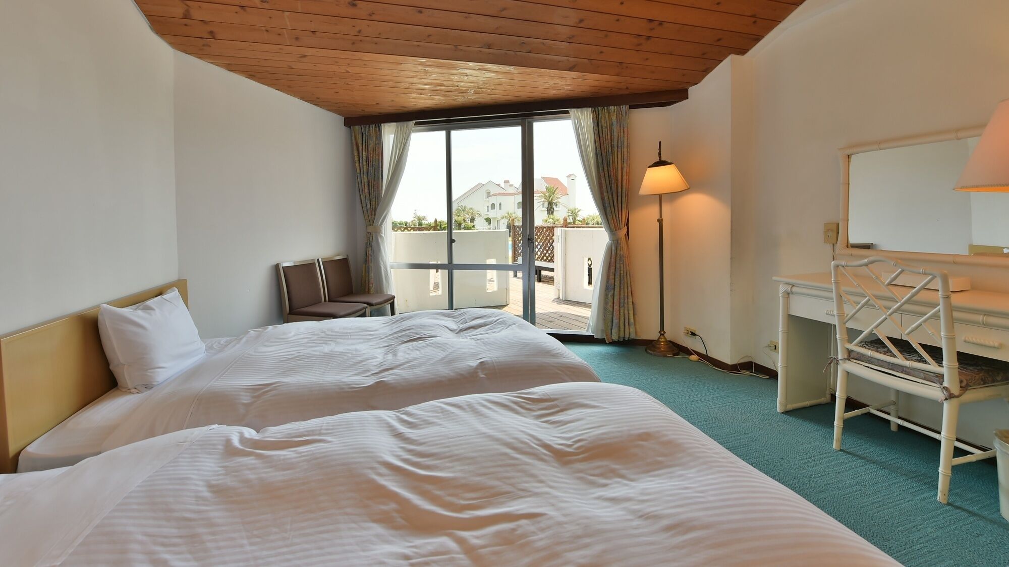Camera d'albergo con due letti, una scrivania, una sedia e un balcone con vista.