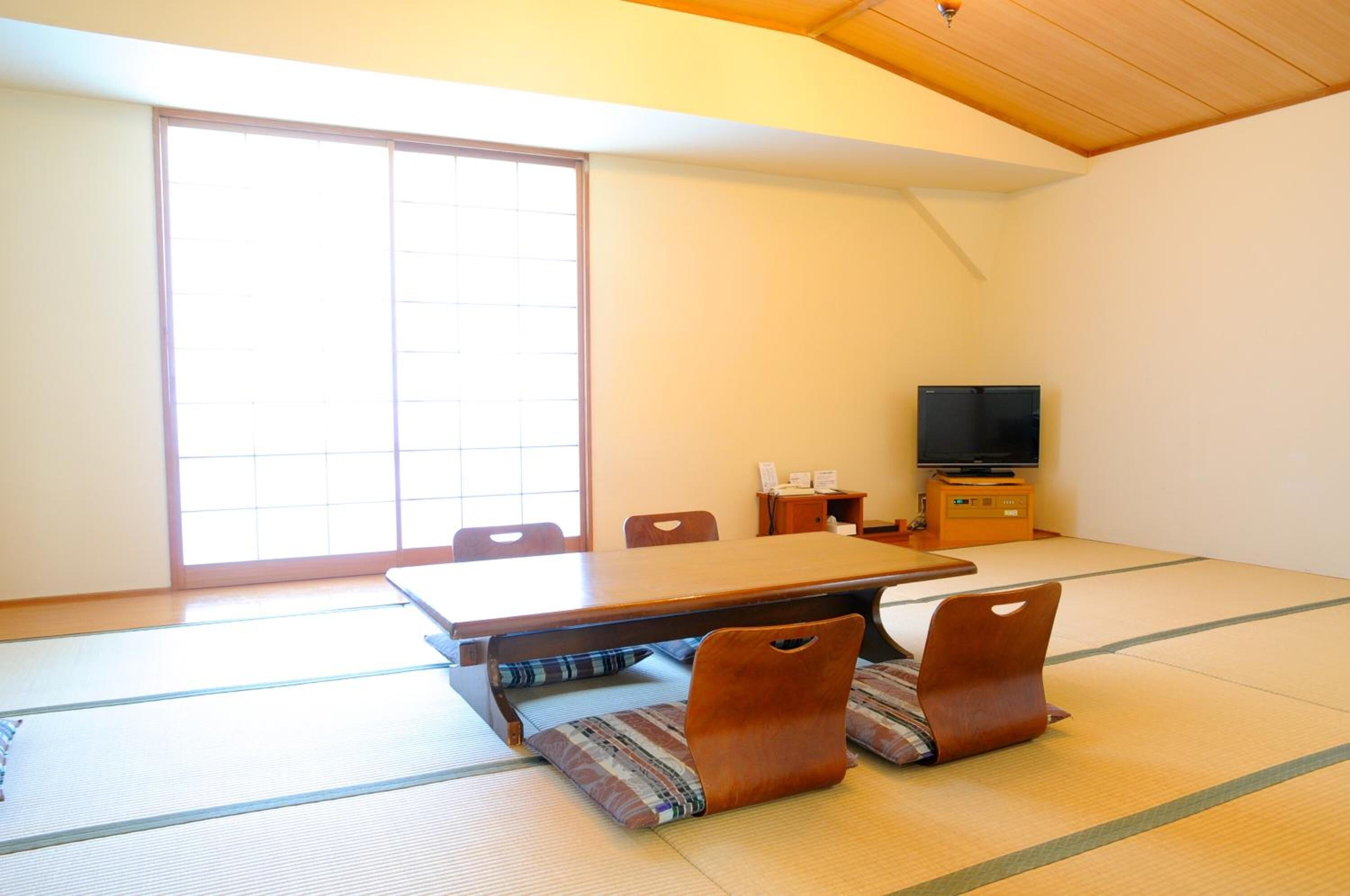 A tatami mat room with a low table, chairs, a television, and a sliding door.