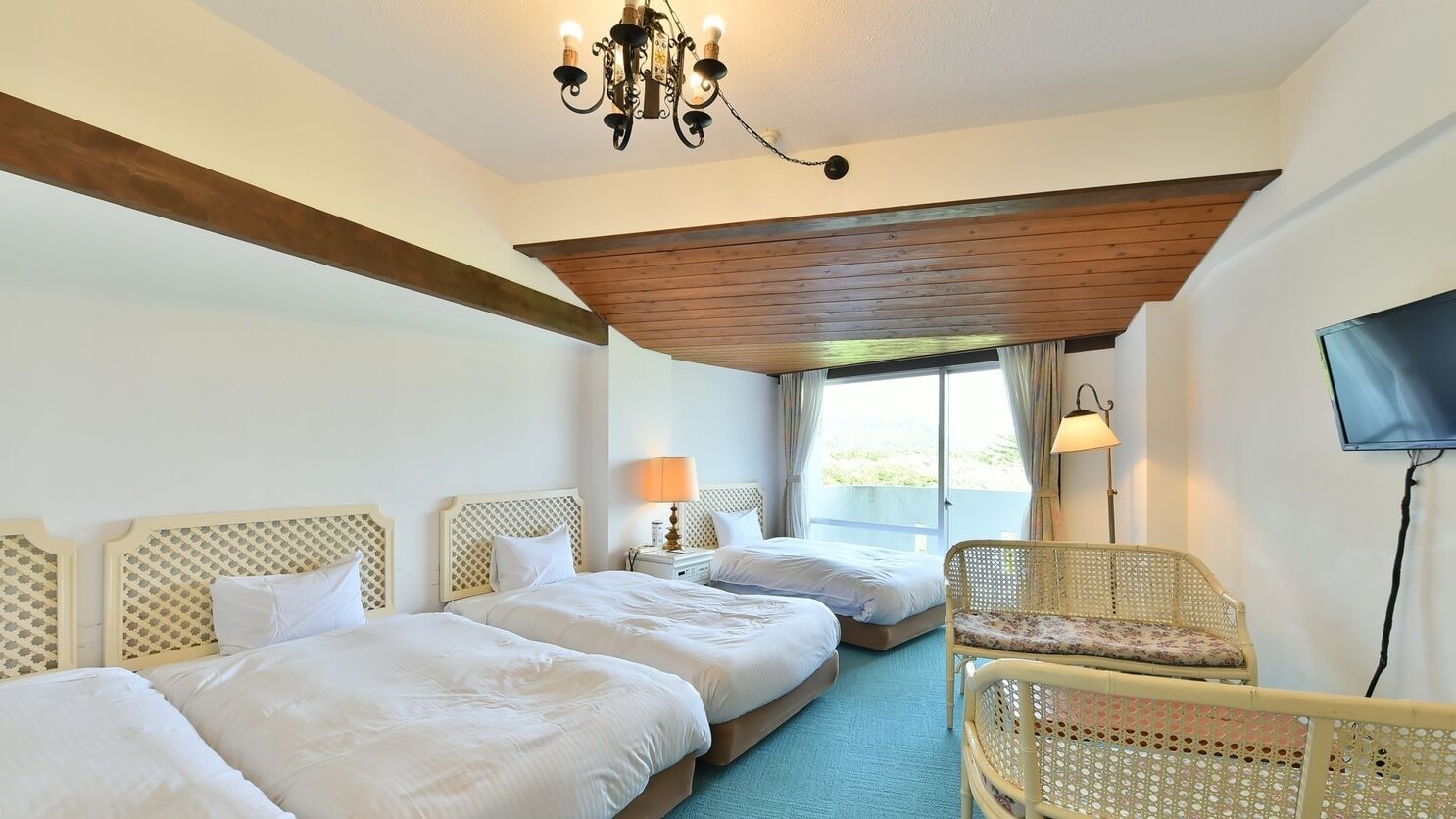 Camera d'albergo con due letti, un lampadario, una televisione e una finestra con tende.