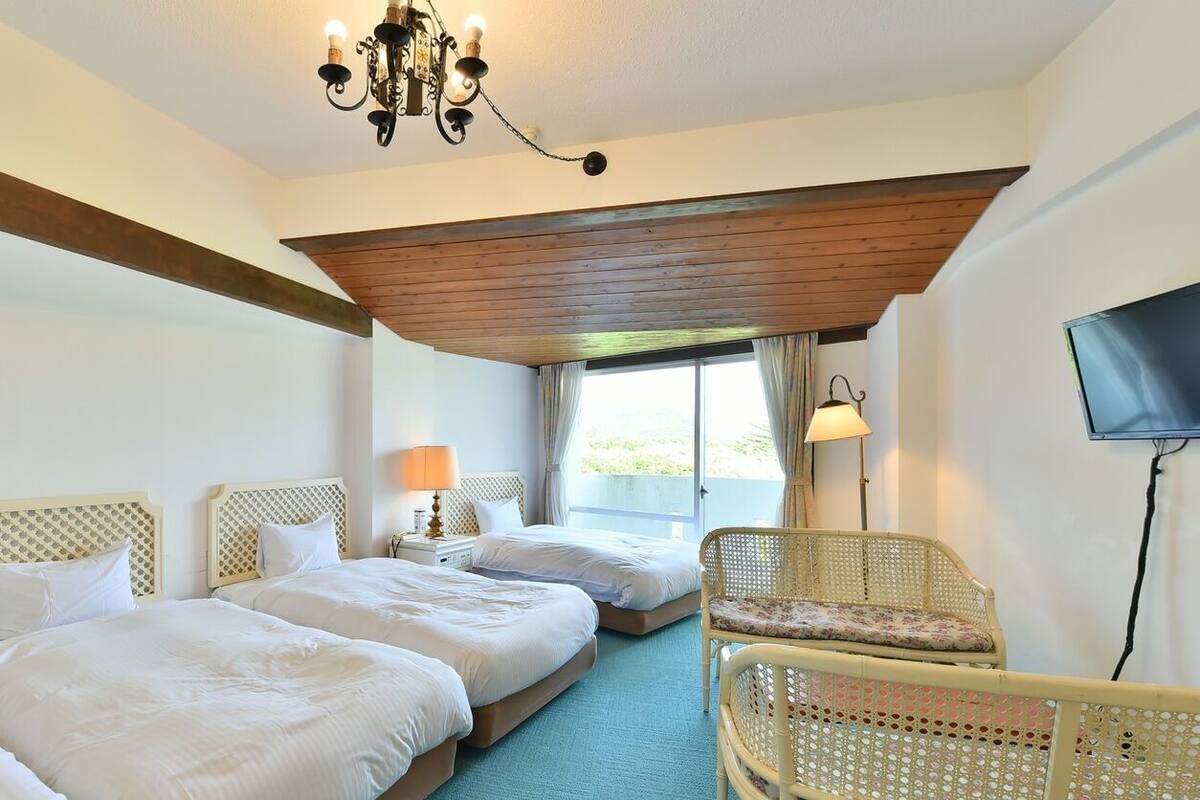 A hotel room with two beds, a chandelier, a television, and a window with curtains.