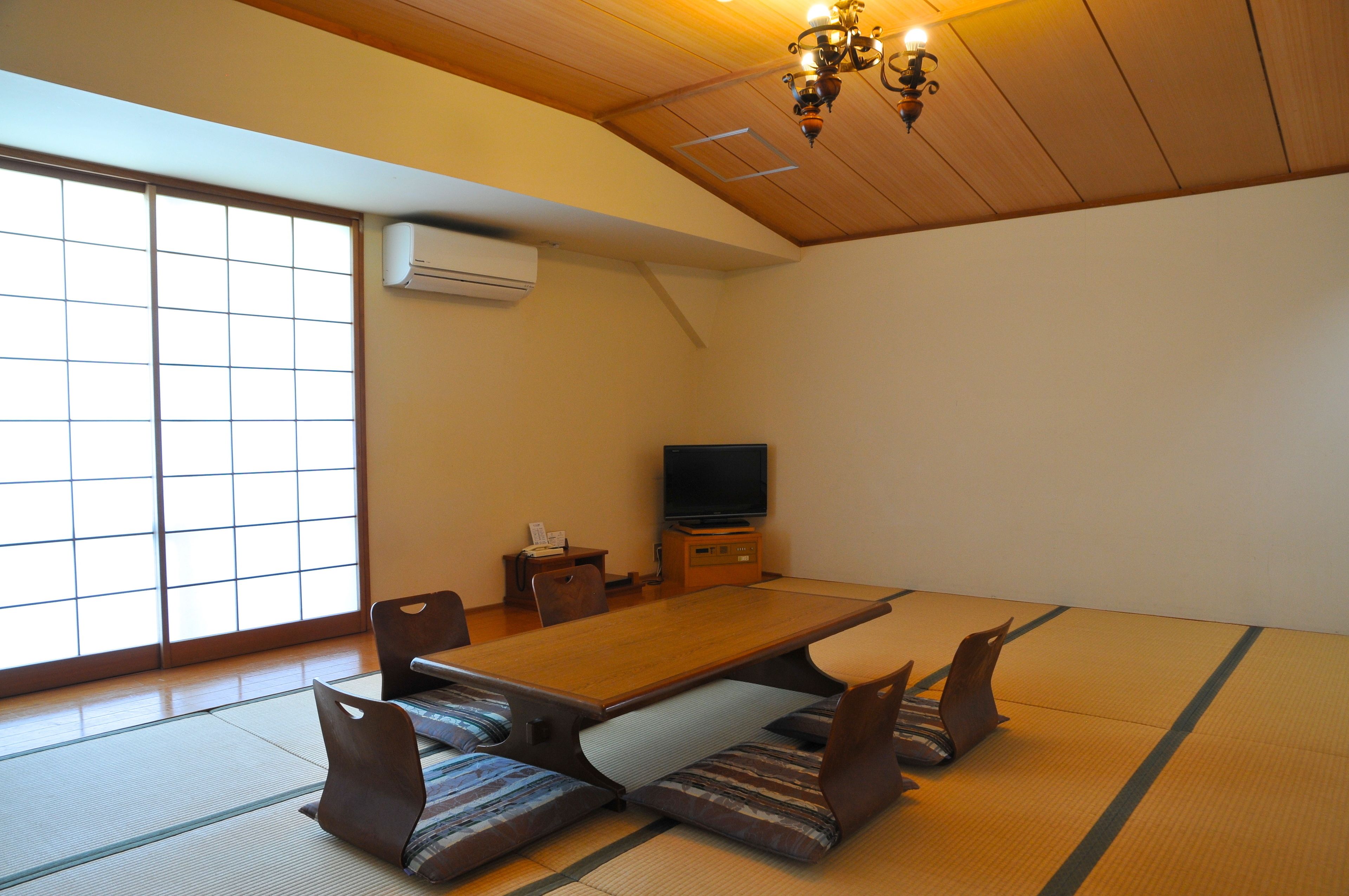 A traditional Japanese room with tatami flooring, a low table, cushions, a television, and sliding doors.
