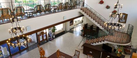 A spacious hotel lobby with a high ceiling, a grand staircase, and a balcony with outdoor seating.