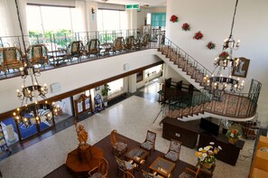 Eine geräumige Hotelhalle mit hoher Decke, einer imposanten Treppe und einem Balkon mit Sitzgelegenheiten im Freien.