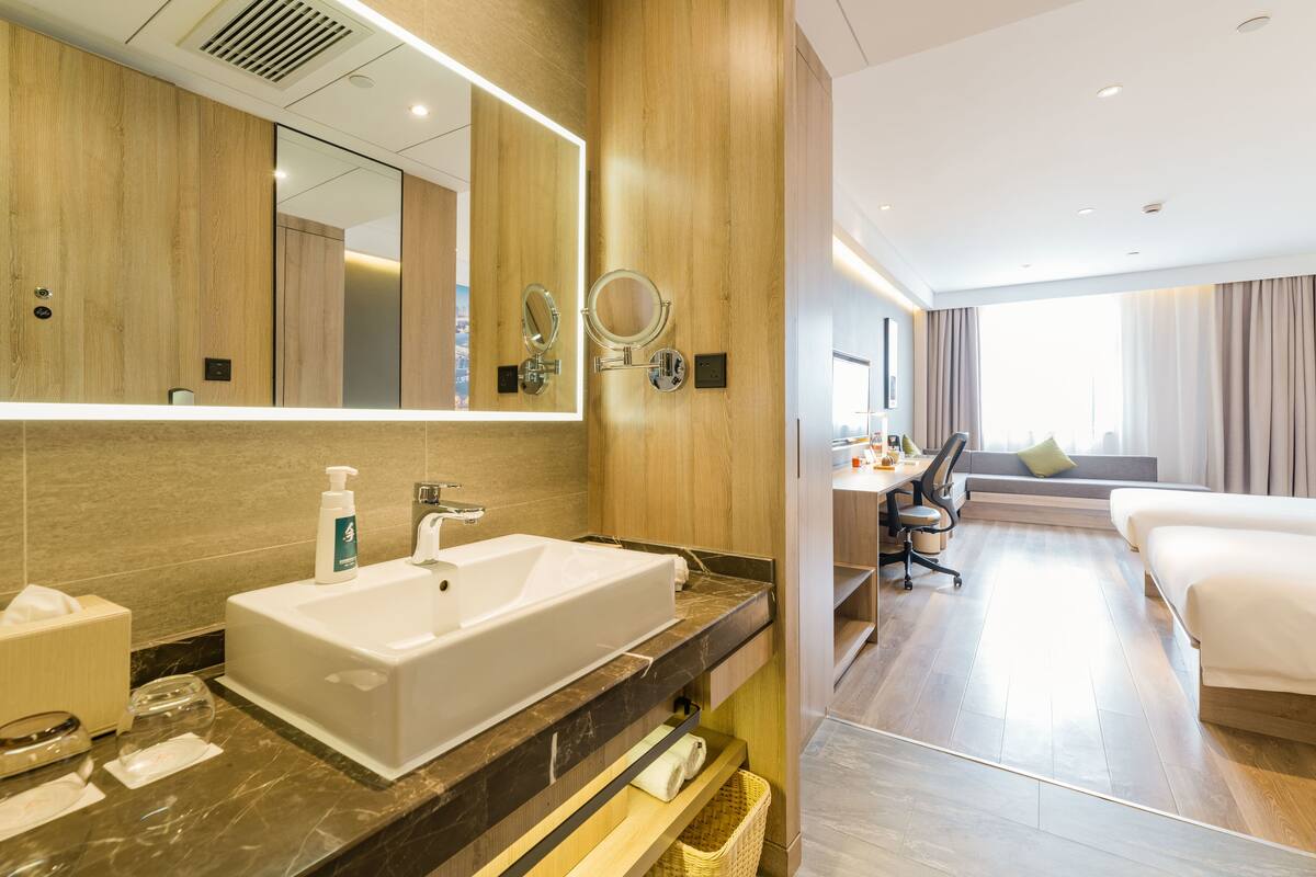 A modern hotel bathroom with a large sink, mirror, and wooden paneling.