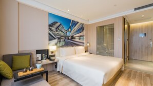 Quarto de hotel moderno com uma cama grande, área de estar com mesa de centro e um mural da paisagem urbana na parede.