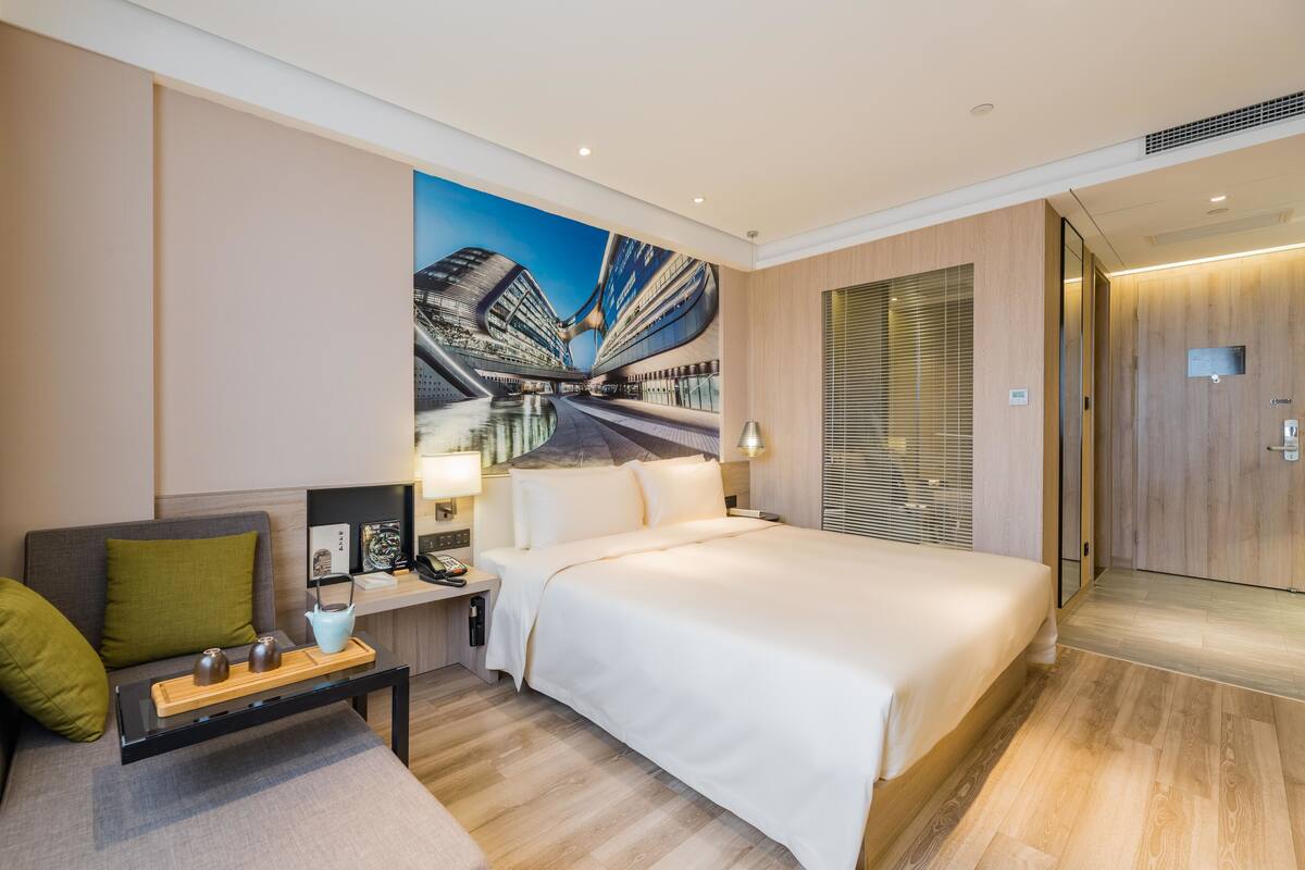 A modern hotel room with a large bed, a seating area with a coffee table, and a cityscape mural on the wall.