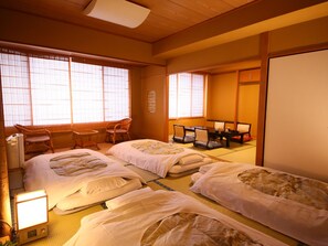 A traditional Japanese-style room with tatami flooring, two tatami beds, a small table with chairs, and a sliding door.