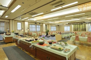 A spacious banquet hall with multiple tables set for dining, a buffet line, and a large window providing natural light.