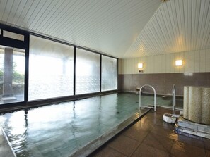 A swimming pool with a glass wall, a metal ladder, and a stone bench.