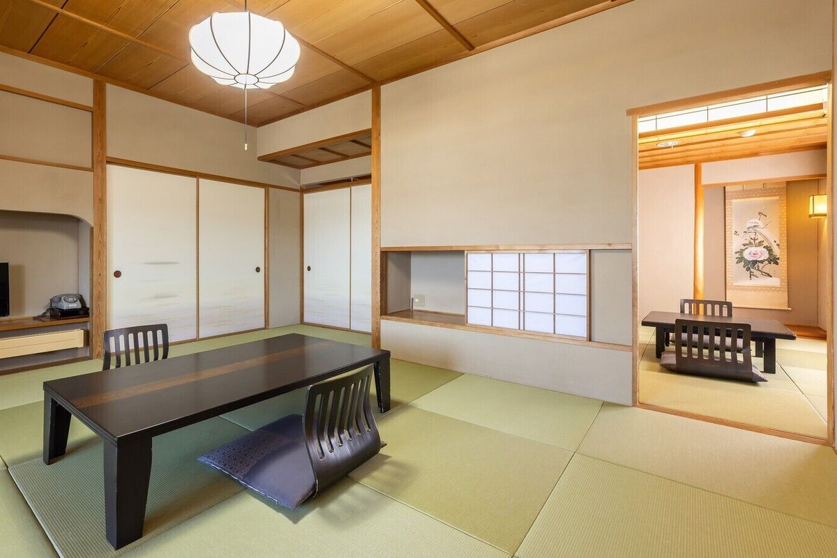 Ett traditionellt japanskt rum med tatamimattor på golvet, ett lågt bord, stolar, en tv och skjutdörrar.