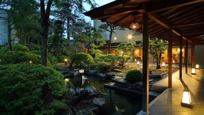 A serene garden with a pond, surrounded by lush greenery and traditional Japanese architecture. - Nunohan (Suwa)