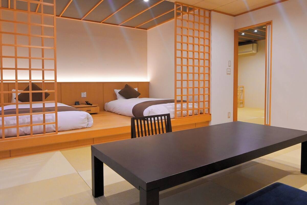 Una habitación tradicional japonesa con dos camas, una mesa baja y puertas correderas.