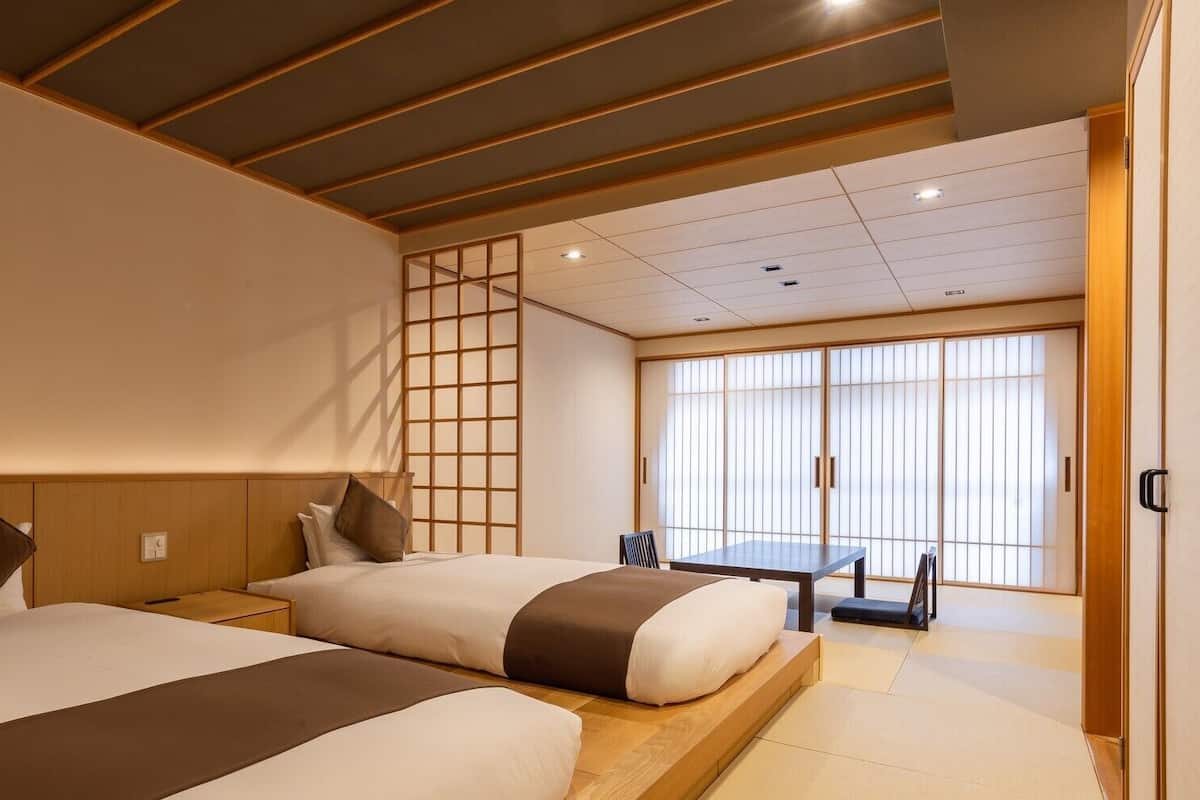 Habitación de hotel con dos camas, una puerta corredera, una mesa y vistas al exterior.