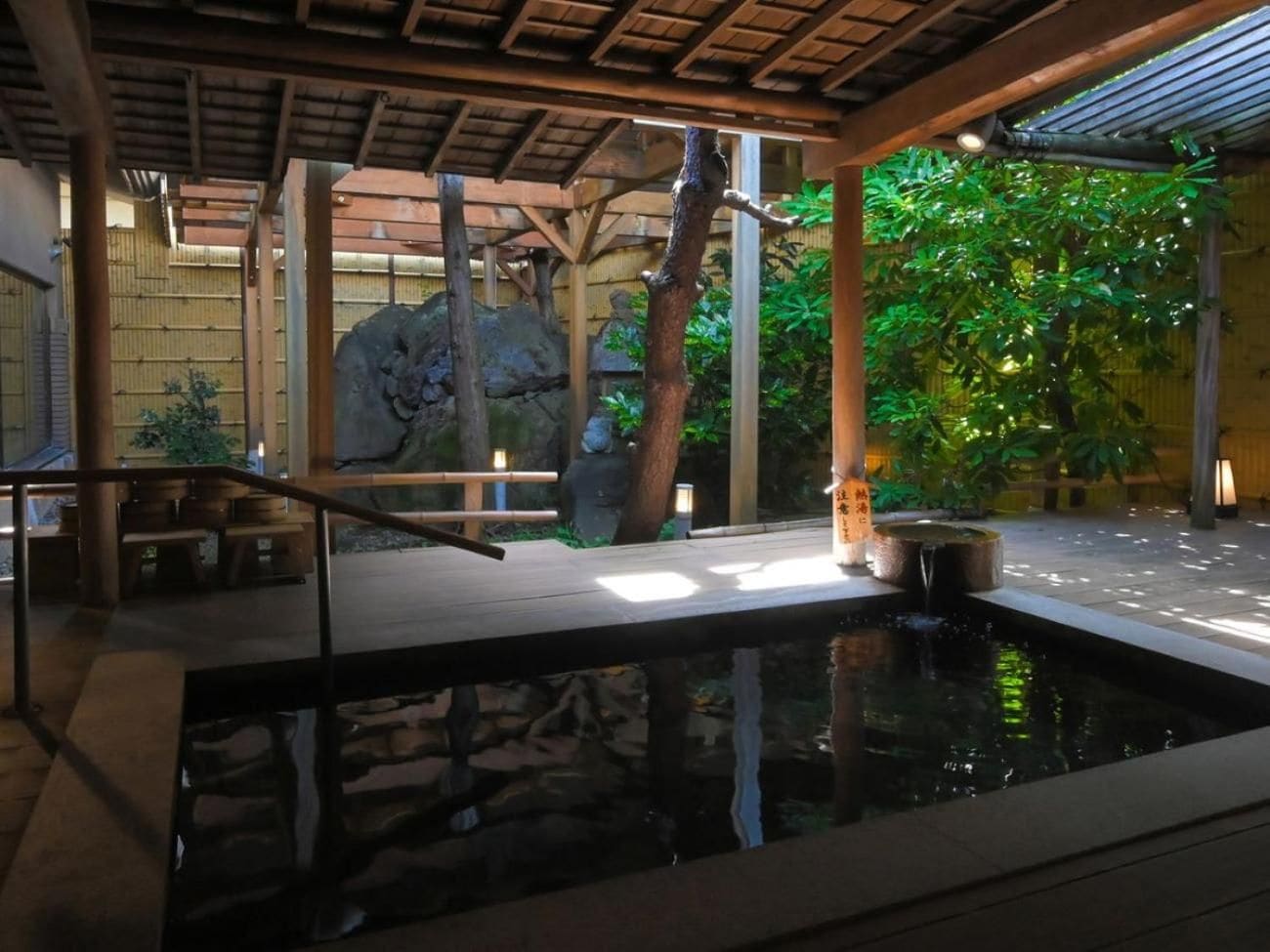 Un jardin intérieur paisible, avec un bassin à carpes koï, des bancs en bois et une sculpture en pierre.